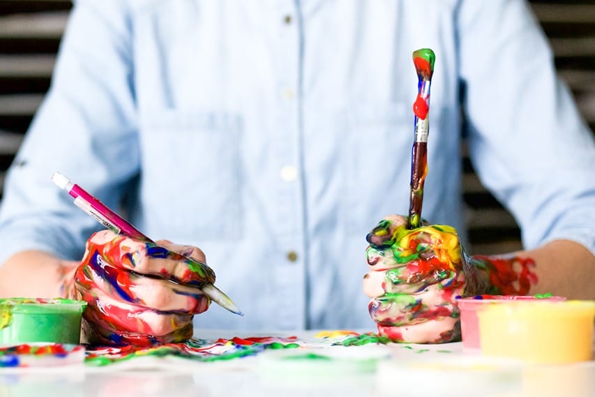 A man holding paintbrushes filled with all the colors, showcasing his creative side